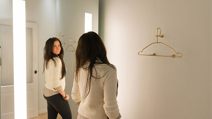 Kundin betrachtet sich im Spiegel, beleuchtet mit AmbiScene Mirror von Philips bei der Lichteinstellung „Tageslicht“