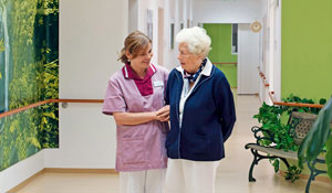 Eine Krankenpflegerin betreut eine ältere Dame in einem erleuchteten Korridor