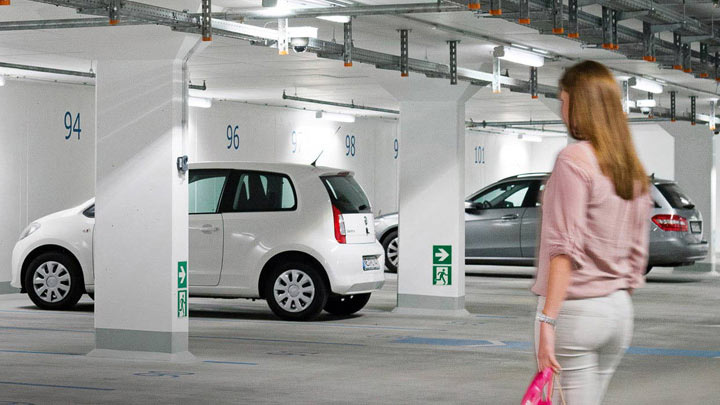 Frau geht in gut beleuchteter Tiefgarage zu ihrem Auto 